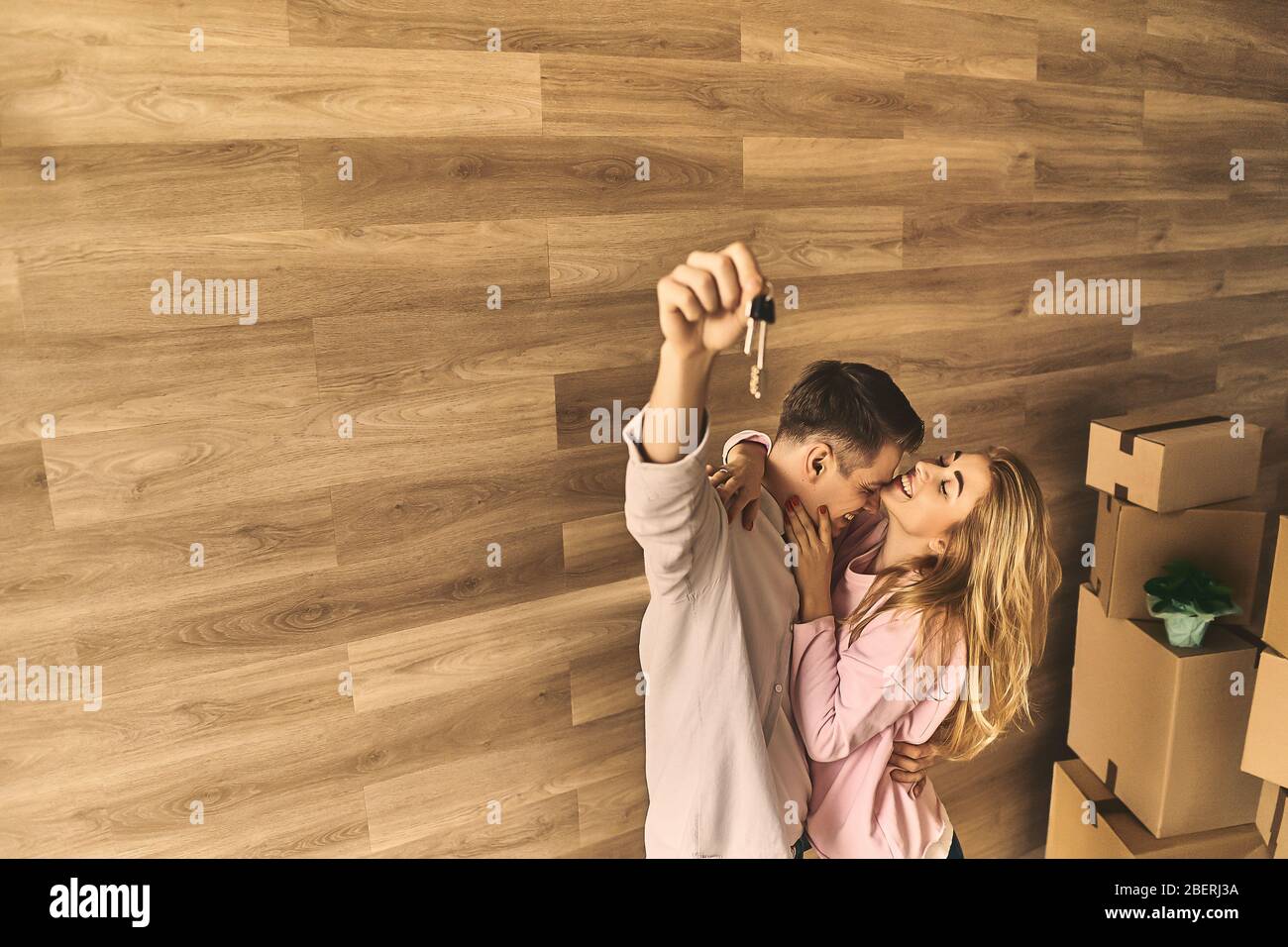 Cheerful girl and happy man moving to new apartment with cardboard boxes and beautiful flowers. Stock Photo