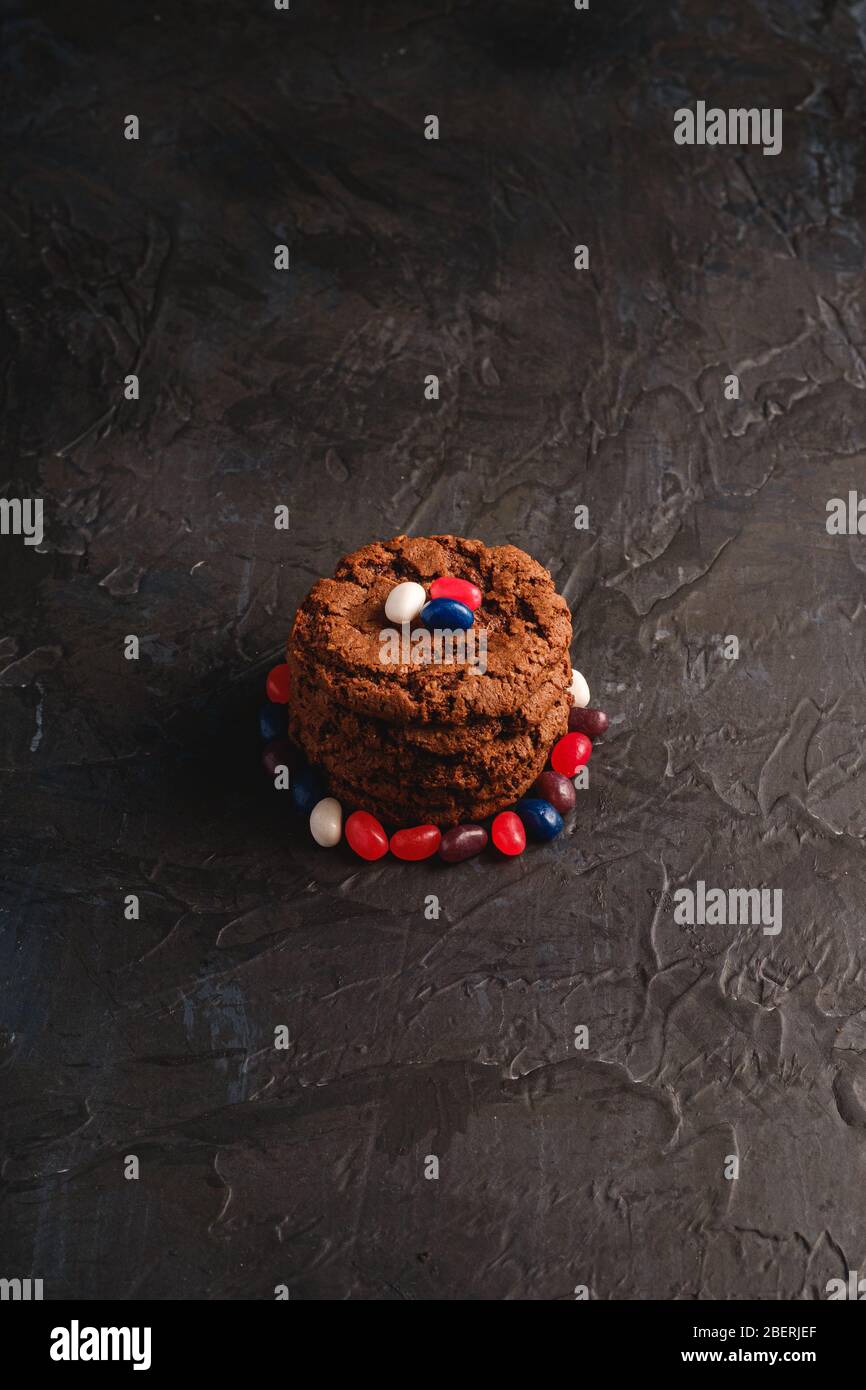 Homemade oat chocolate cookies stack with cereal with juicy jelly beans on textured dark black background, angle view Stock Photo