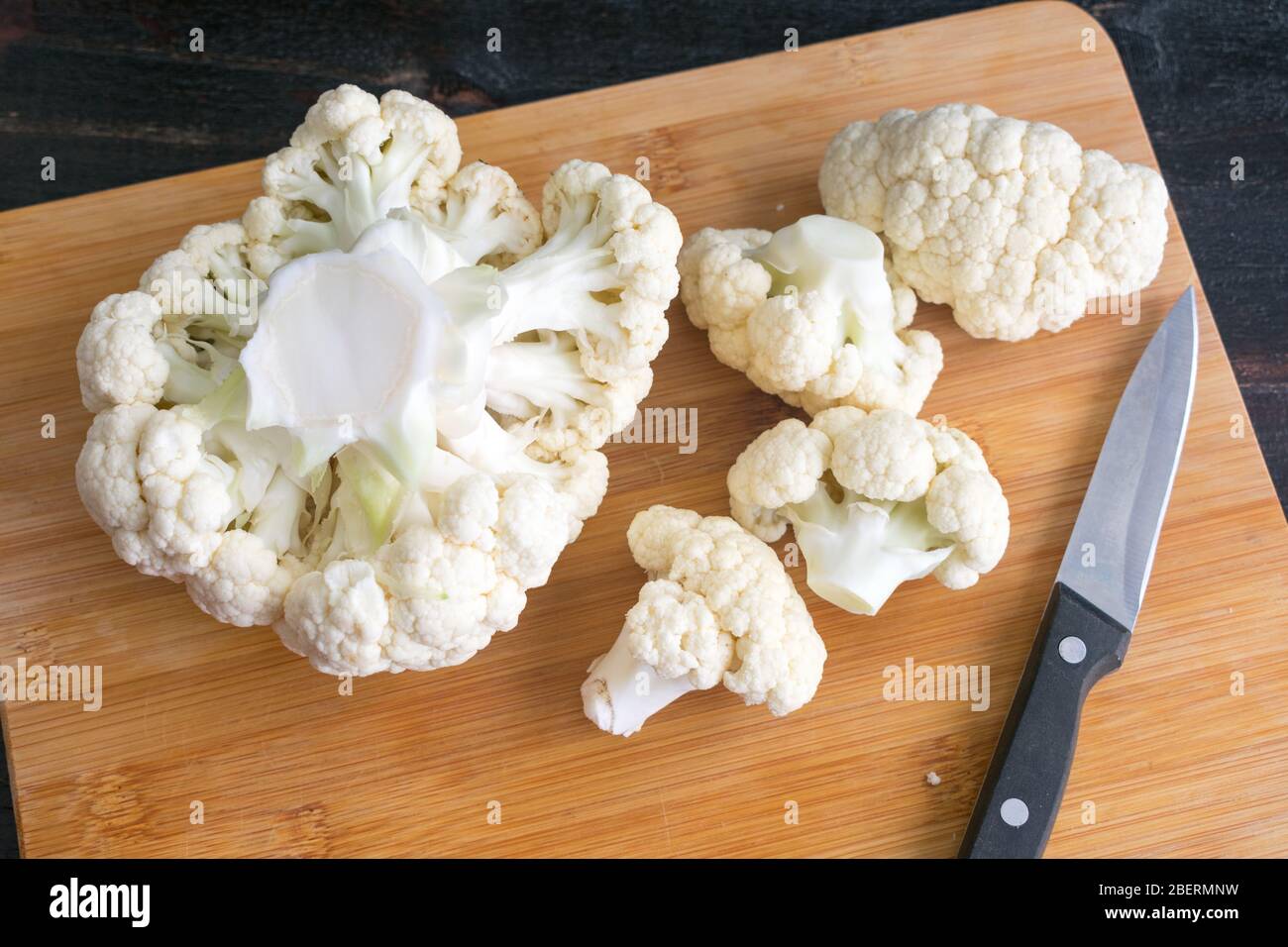 Cutting a Head of Cauliflower into Florets: Cauliflower on a bamboo cutting board with a paring knife Stock Photo