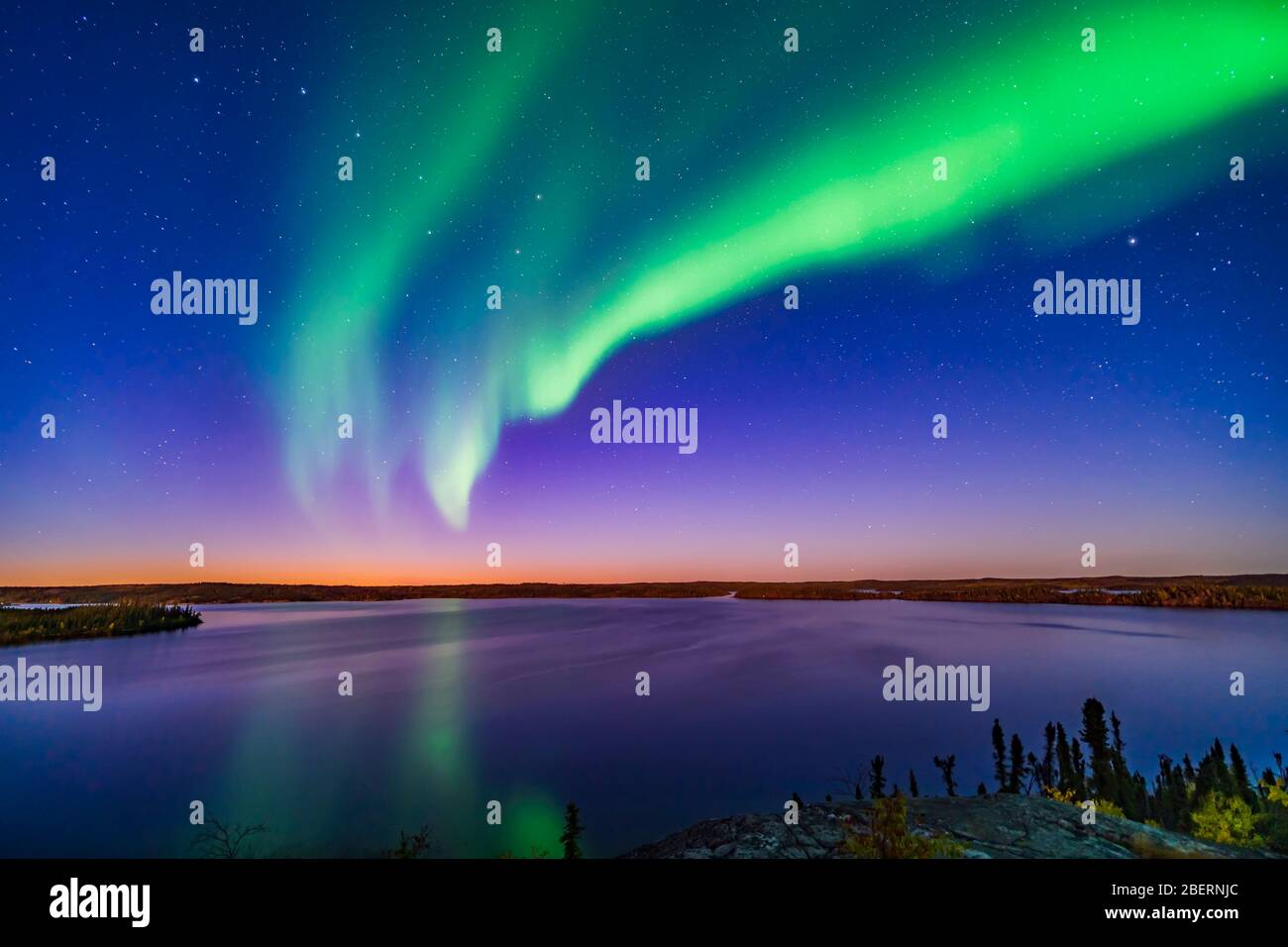 An arc of northern lights appears in the evening twilight over Prelude Lake, Canada. Stock Photo