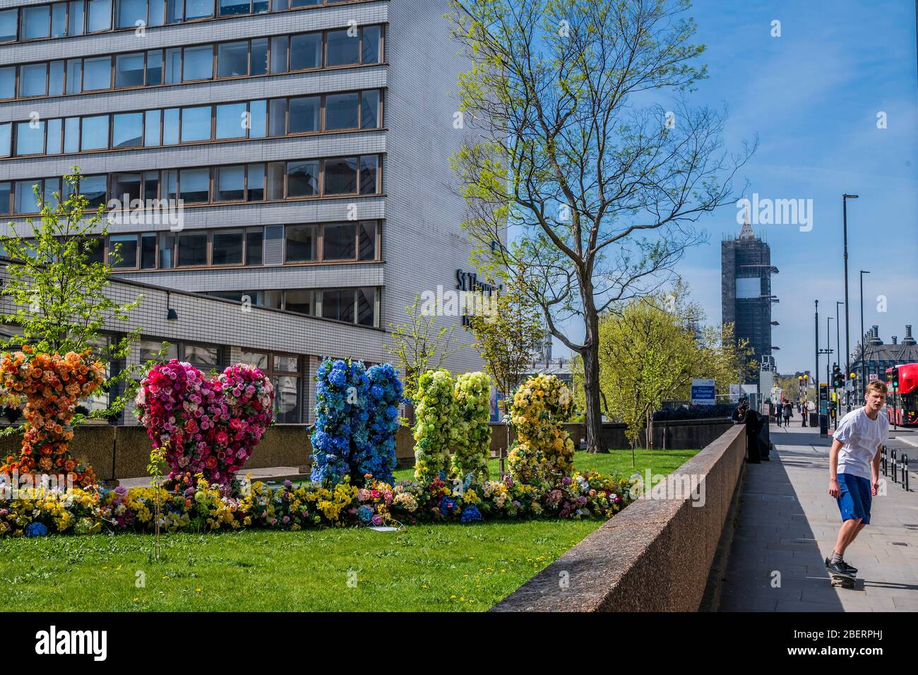 London, UK. 15th Apr, 2020. Passers by admire and photograph a floral Tribute, which spells 'I Love (heart) NHS', outside St Thomas' Hospital - The 'lockdown' continues in London because of the Coronavirus (Covid 19) outbreak. Credit: Guy Bell/Alamy Live News Stock Photo