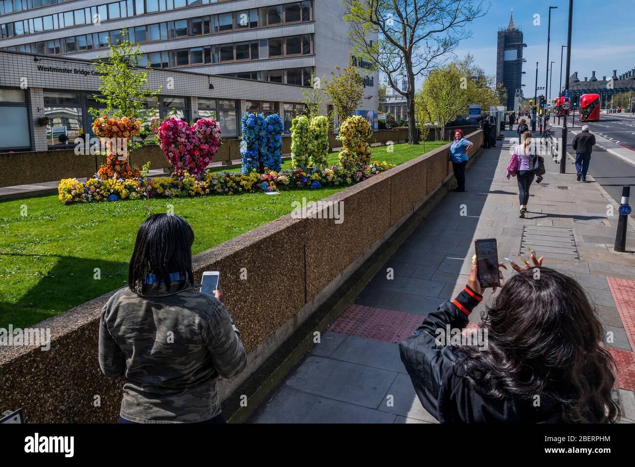 London, UK. 15th Apr, 2020. Passers by admire and photograph a floral Tribute, which spells 'I Love (heart) NHS', outside St Thomas' Hospital - The 'lockdown' continues in London because of the Coronavirus (Covid 19) outbreak. Credit: Guy Bell/Alamy Live News Stock Photo