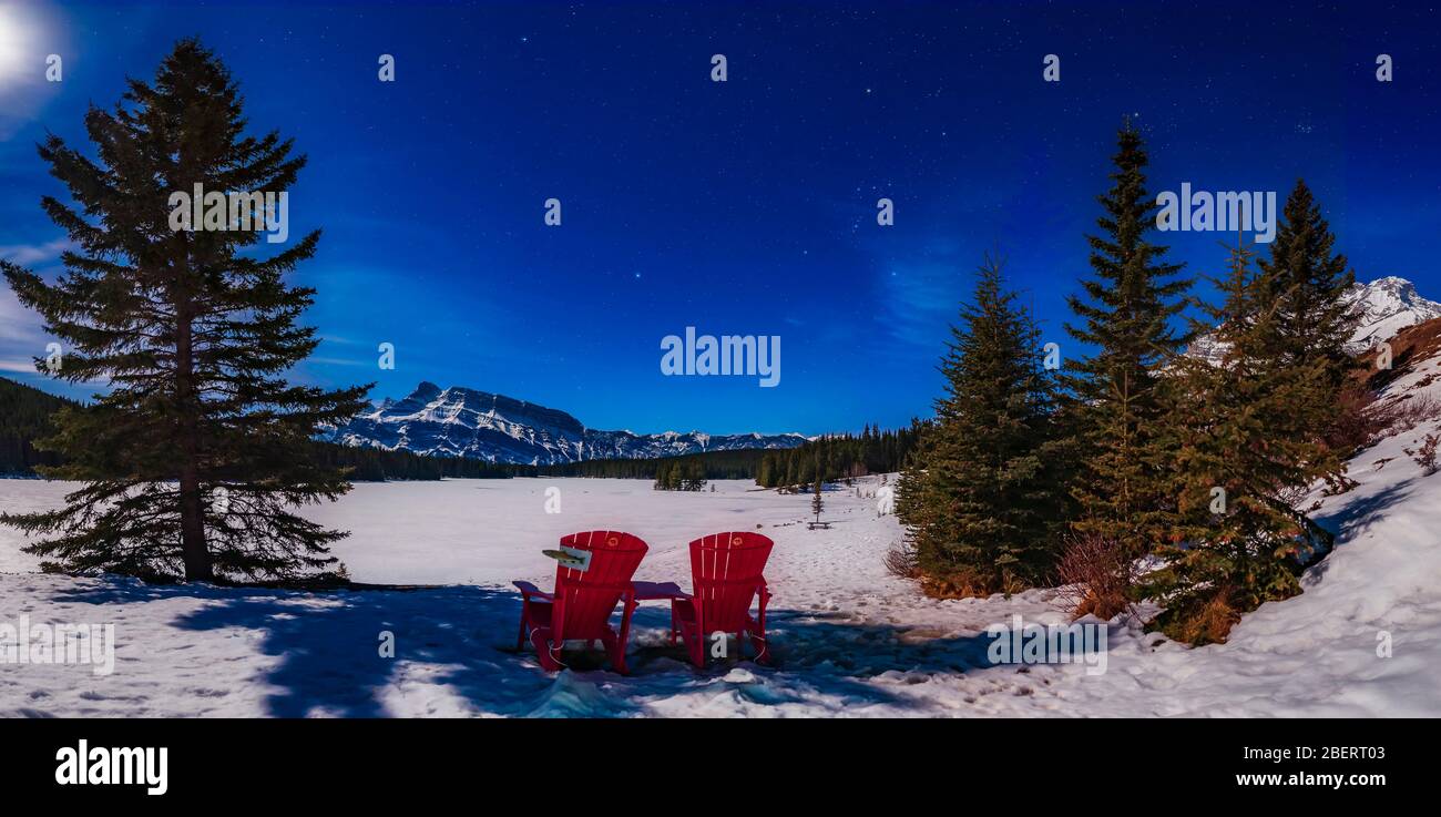 Red chairs under a moonlit winter sky at Two Jack Lake, Banff National Park, Canada. Stock Photo