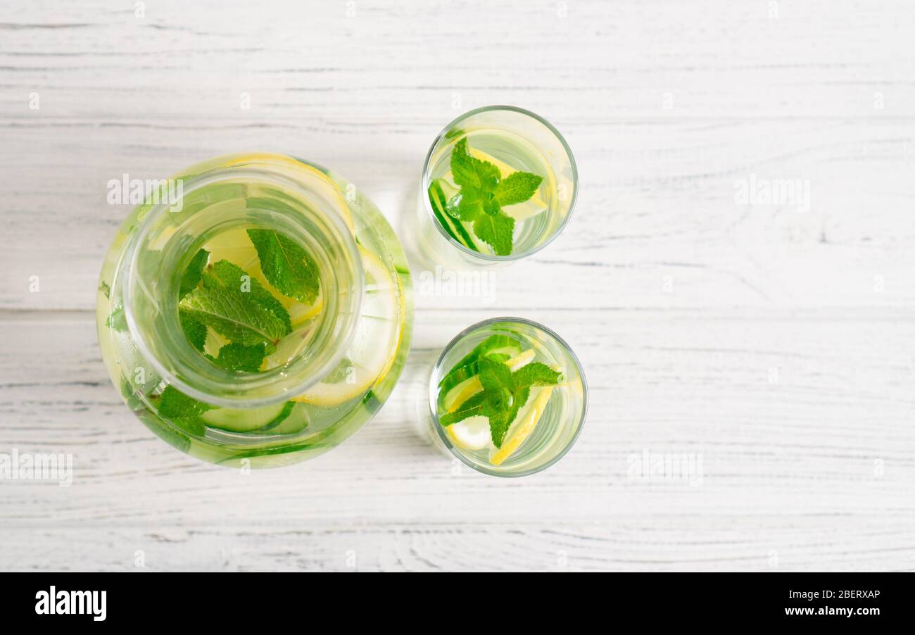 Top view of light and fresh cucumber, lemon and mint drink in jar and glasses on white table. Detox water. Stock Photo