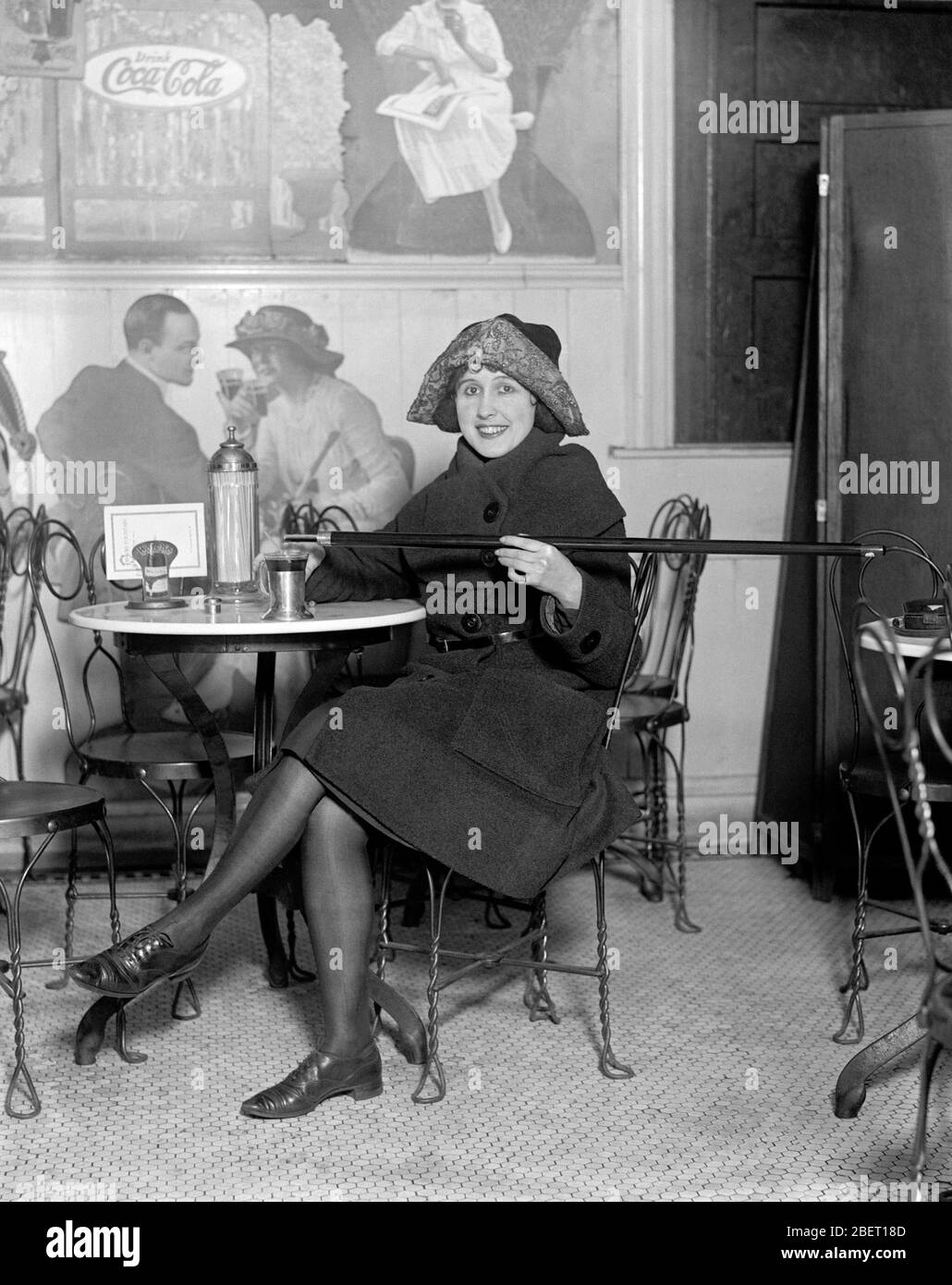 A flapper sitting in a restaurant pouring alcohol into a cup from a cane during Prohibition. Stock Photo
