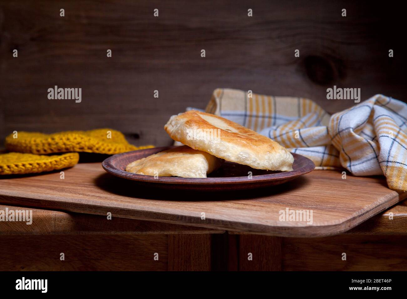 Clay plate with two of individual fried pies with meat on wooden table. Tatar traditional pies. Stock Photo