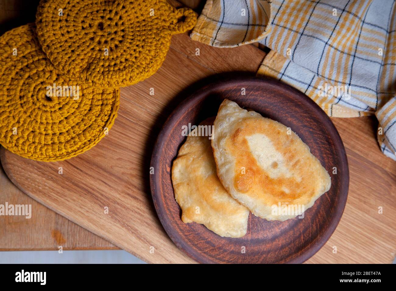 Clay plate with two of individual fried pies with meat on wooden table. Tatar traditional pies. Stock Photo