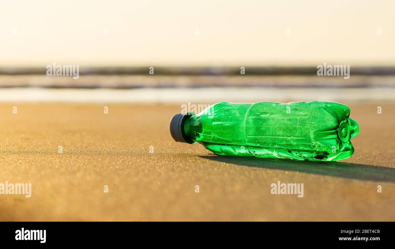 A green plastic bottle laying on the beach sand Stock Photo
