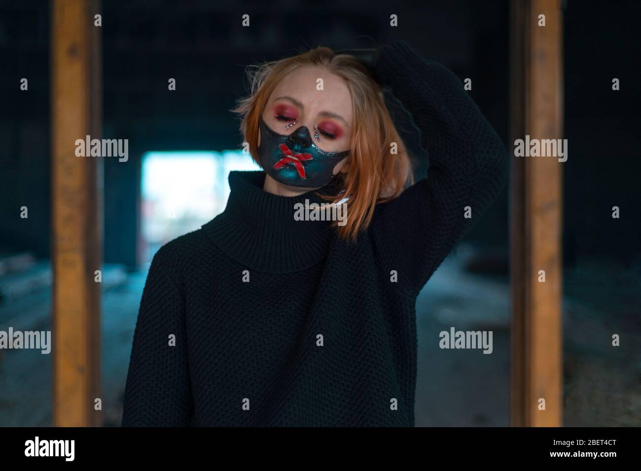 Closeup beauty portrait of a beautiful girl in a black mask with rhinestones, designer makeup. Emotionally posing. Against the background of the destr Stock Photo