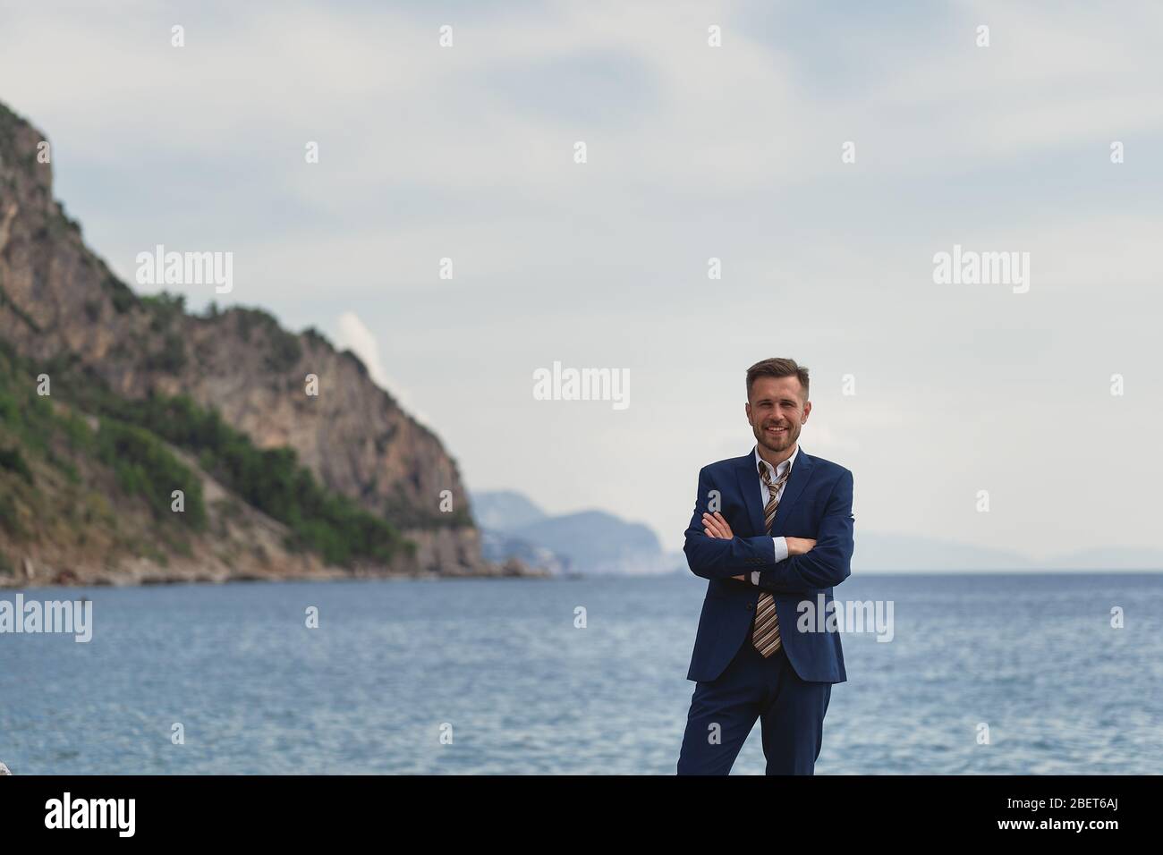 Businessman standing on the beach in a suit a untied tie. He looks at ...