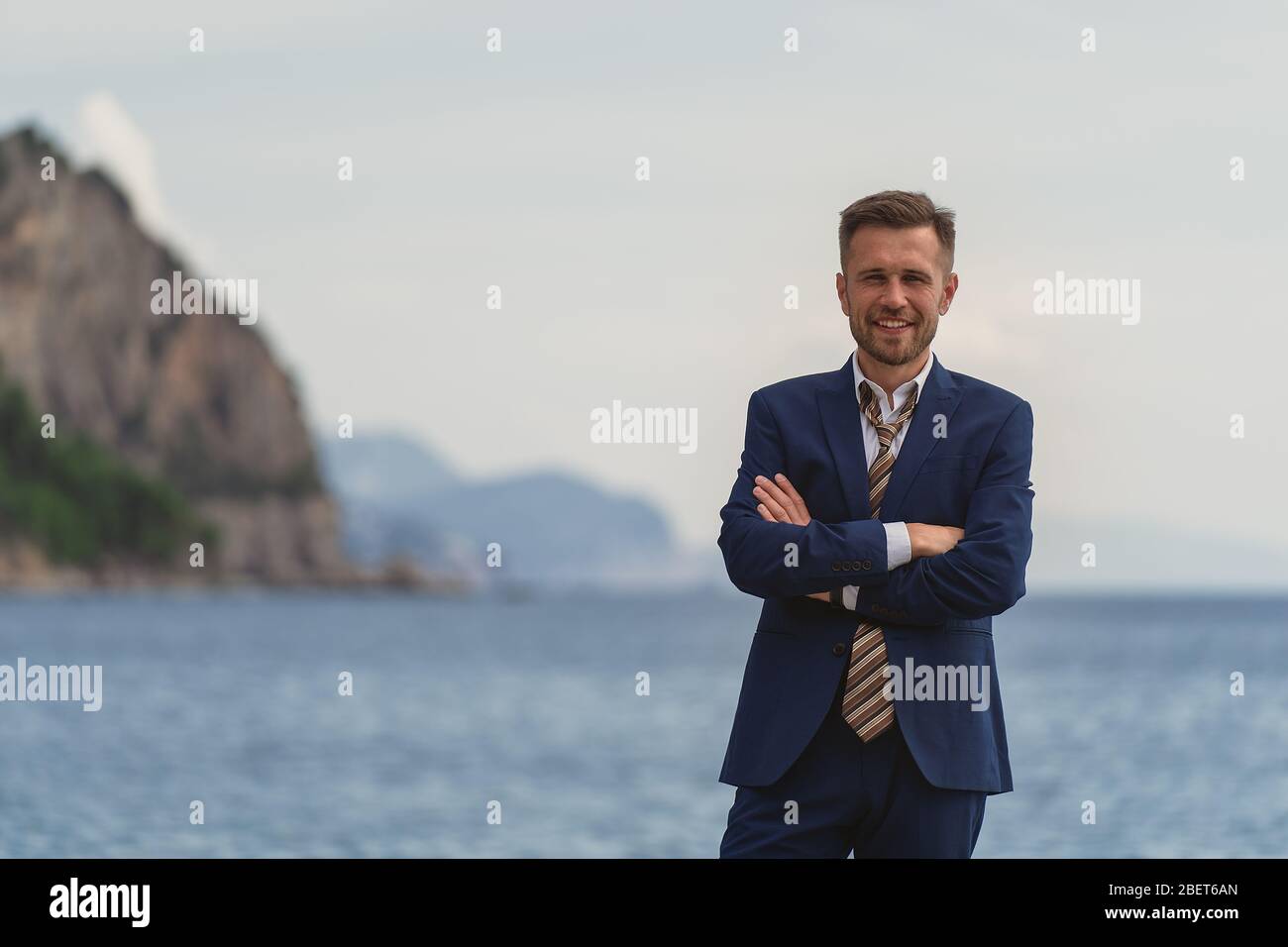 Businessman standing on the beach in a suit a untied tie. He looks at ...