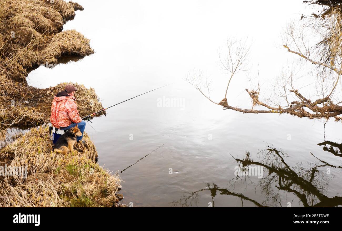 fisherman with a dog fishes in the river Stock Photo