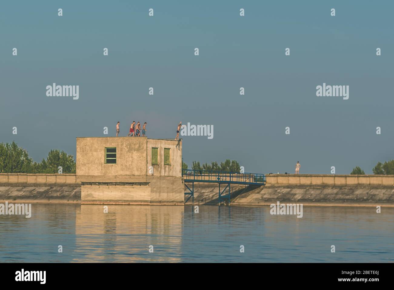 brave boys jumping from the roof of the building in the rocky barrier into the blue water of rural ponde Stock Photo