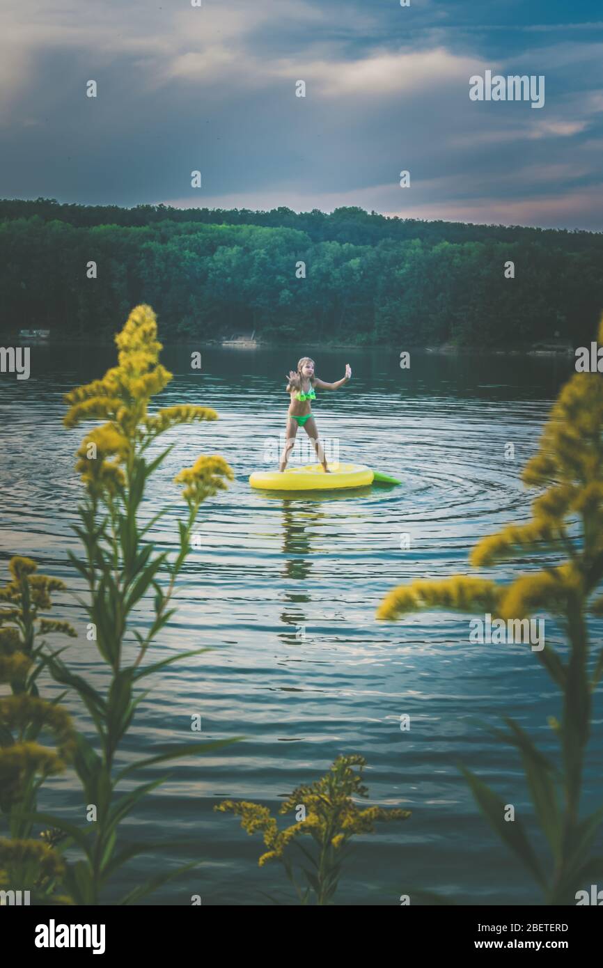scenic view to yellow flowers and girl having fun in rural pond in colorful sunset Stock Photo