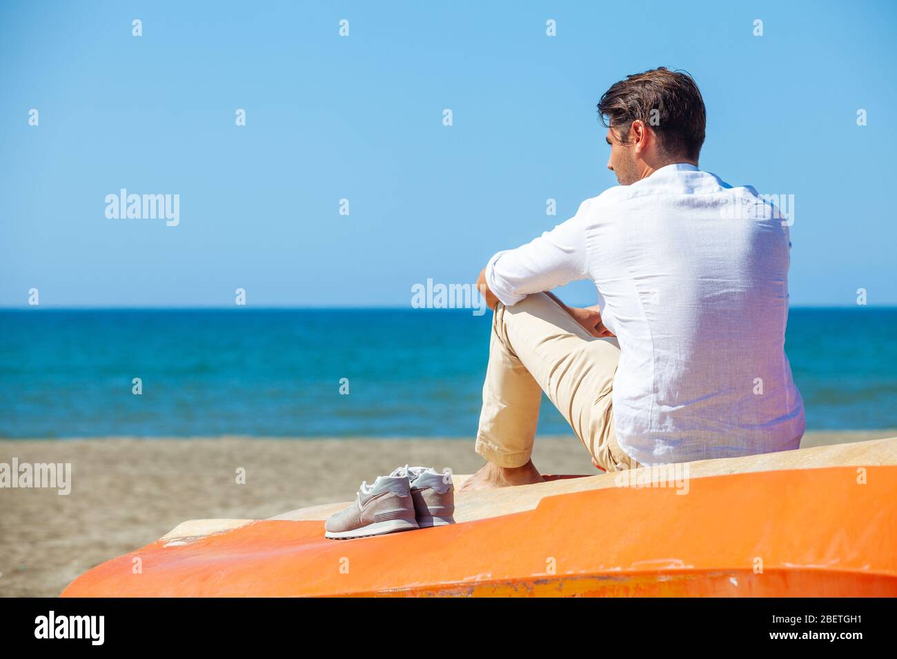 Lonely man on the beach above a boat looking at the sea. Seated ...
