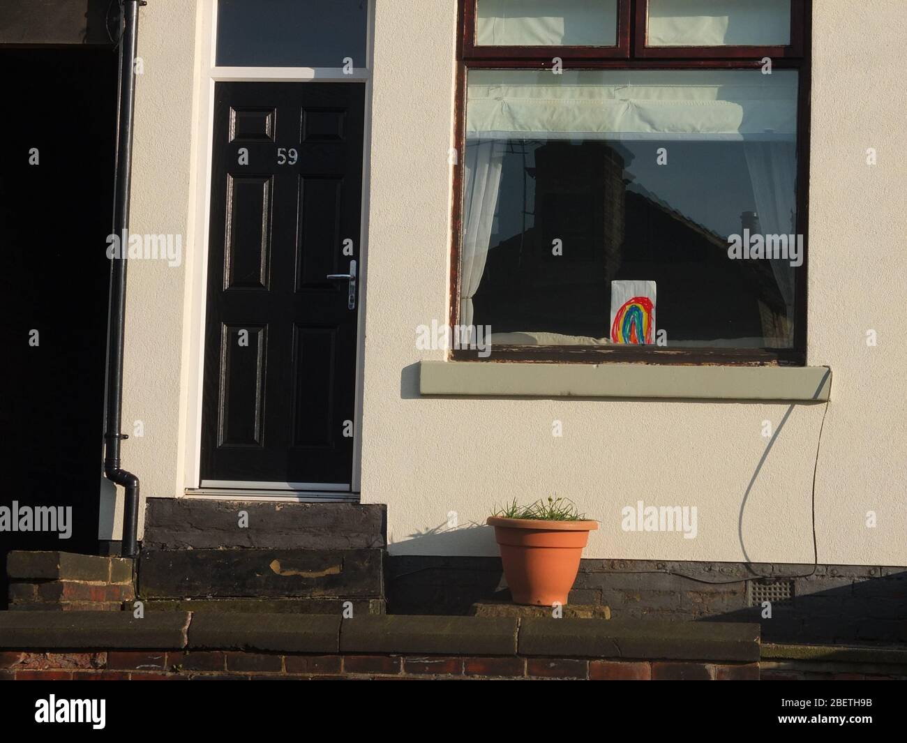 A colourful child's drawing of a rainbow in a house window during the UK Coronavirus Crisis and Lockdown signifying a message of hope for the future Stock Photo