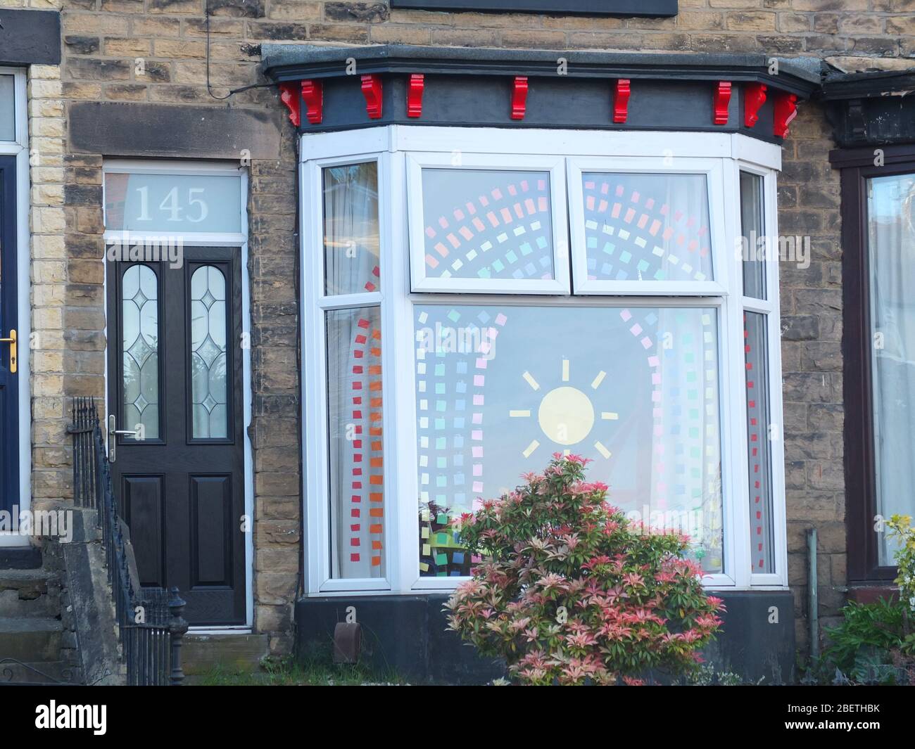 Display of cut coloured paper forming the symbol of a rainbow and sunshine as message of hope during the Coronavirus crisis in bay window of UK house Stock Photo