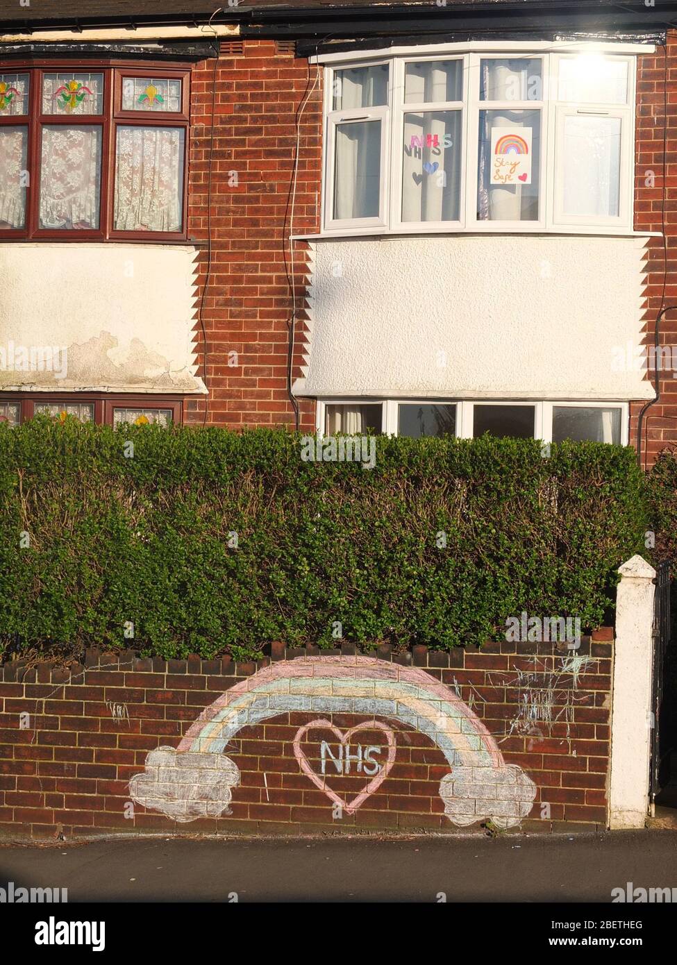 A chalked rainbow and message of support and gratitude to the NHS on the front wall of a house in Sheffield UK also with rainbows in upstairs window. Stock Photo