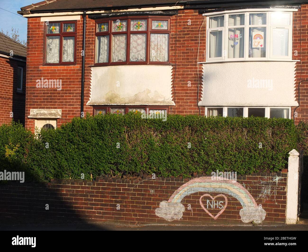 A chalked rainbow and message of support and gratitude to the NHS on the front wall of a house in Sheffield UK also with rainbows in upstairs window. Stock Photo
