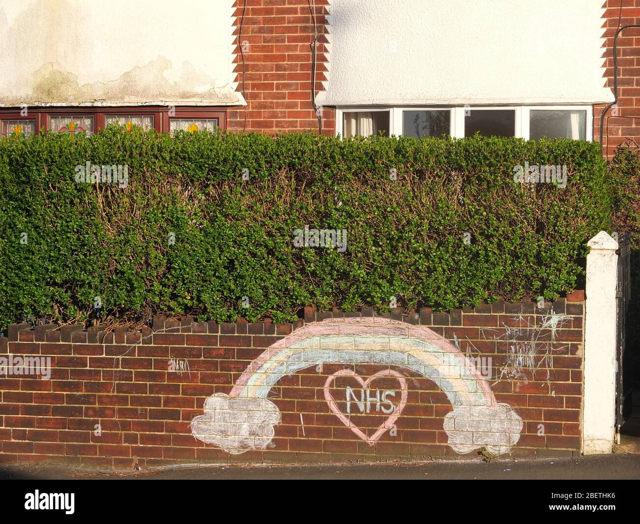A chalked rainbow and message of support and gratitude to the NHS on the front wall of a house in Sheffield UK also with rainbows in upstairs window. Stock Photo