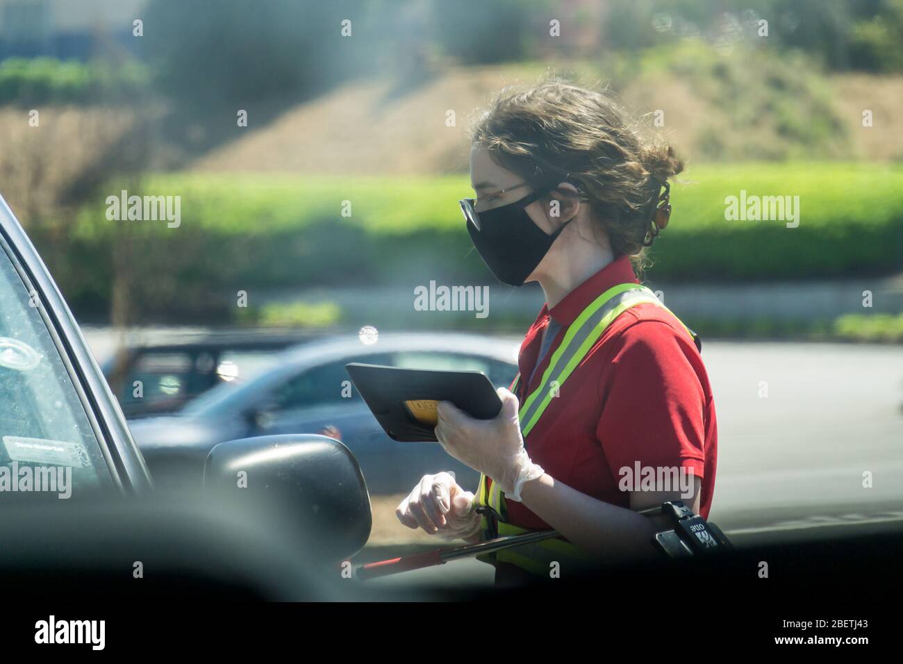 Kennesaw, GA / USA - 04/02/20: Young youthful fast food worker working at Chick-fil-a drive through amidst cars take orders with tablet. Stock Photo