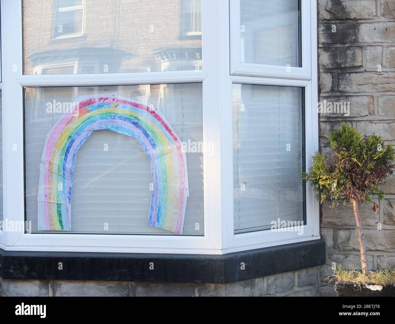 A colourful child's drawing of a rainbow in a house window during the UK Coronavirus Crisis and Lockdown signifying a message of hope for the future Stock Photo