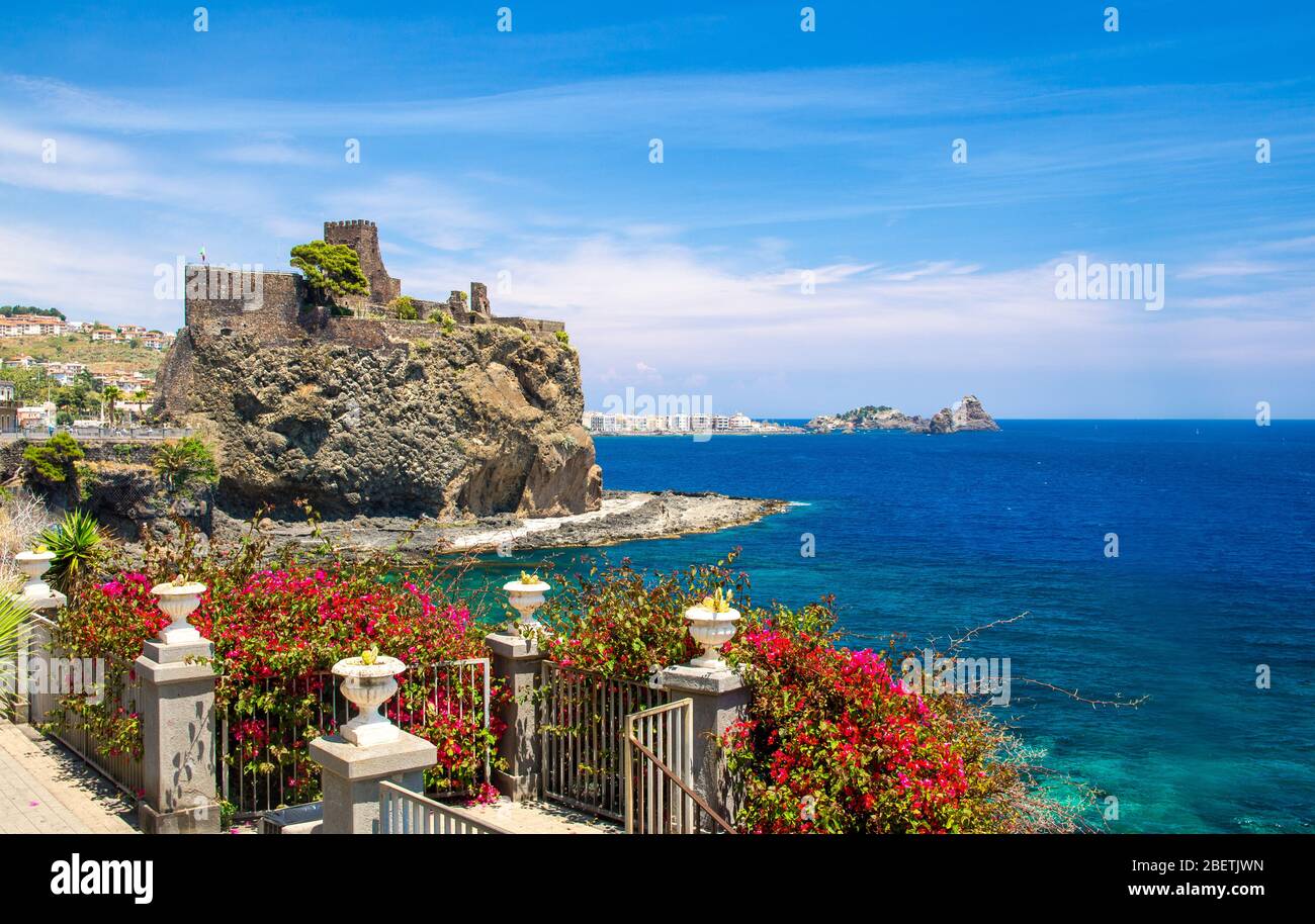 Norman old medieval Castle Aci Castello with stone walls on rock coast near  water of mediterranean sea and fence with red flowers foreground, Catania  Stock Photo - Alamy