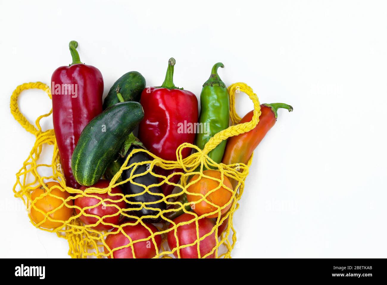 Fresh organic vegetables in a yellow shopping mesh bag on white background, horizontal format, Zero waste concept, Copy space Stock Photo