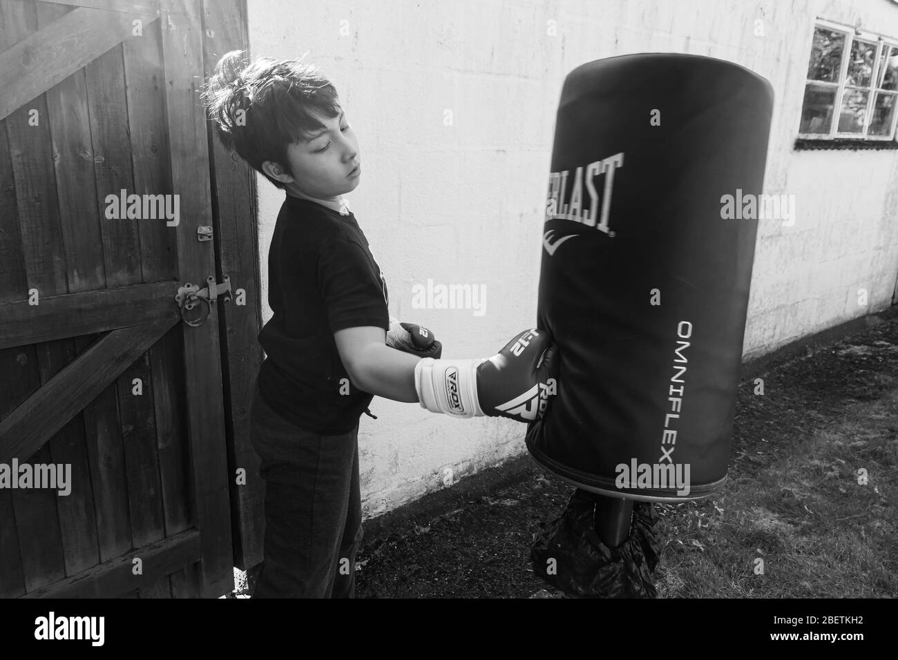 A young boy wearing boxing gloves punch a punching bag in the garden for exercise. Stock Photo