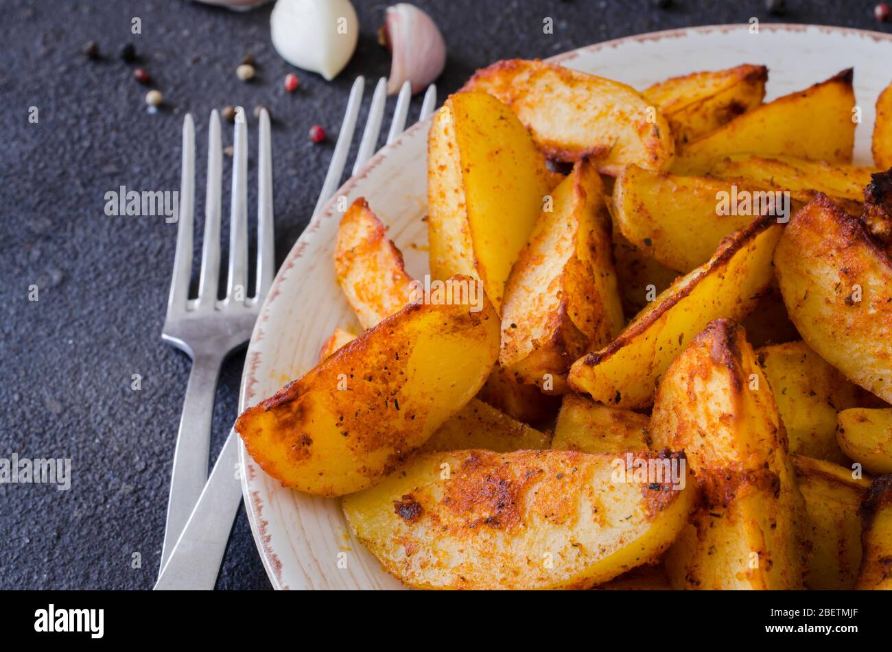 Golden spicy potato wedges fried or oven baked with garlic in plate on dark  table. Delicious savoury crisp snack in rustic style. Top view Stock Photo  - Alamy