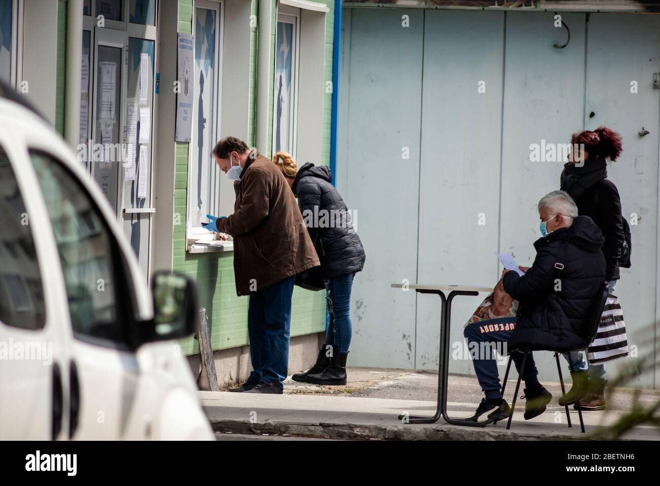 Sofia, Bulgaria. 15 April 2020. Unemployed people wearing protective face masks waiting and filling out forms on impromptu social distancing small tables outside a local job centre of the Department for Social Protection. The unemployment in the country has risen to 7% because of the Pandemic Coronavirus Covid - 19 after years of stable low rates at around 3.5%. Stock Photo