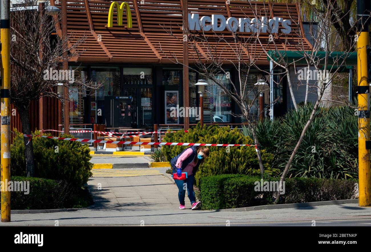 Woman wearing protective face mask in front of closed for normal business McDonald's fast food restaurant due to the spread of the Coronavirus Pandemic of Covid-19 in Sofia, Bulgaria as of 2020 Stock Photo