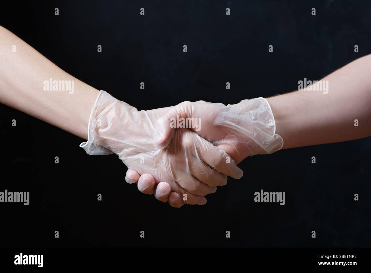 Handshake in medical gloves on black background. Partial view. Stock Photo