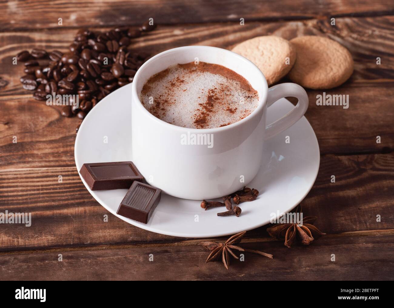 a cap of coffee with foam, cakes,  heart-shaped coffee beans on the wooden table.  Flat Lay with no people Stock Photo