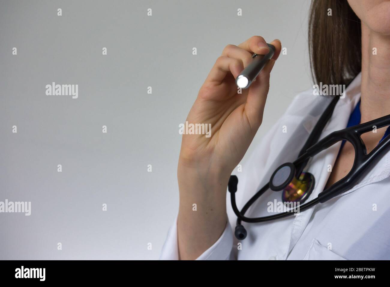 Medical professional with pen light isolated on grey background. Stethoscope and white coat visible. Room for type and copy Stock Photo