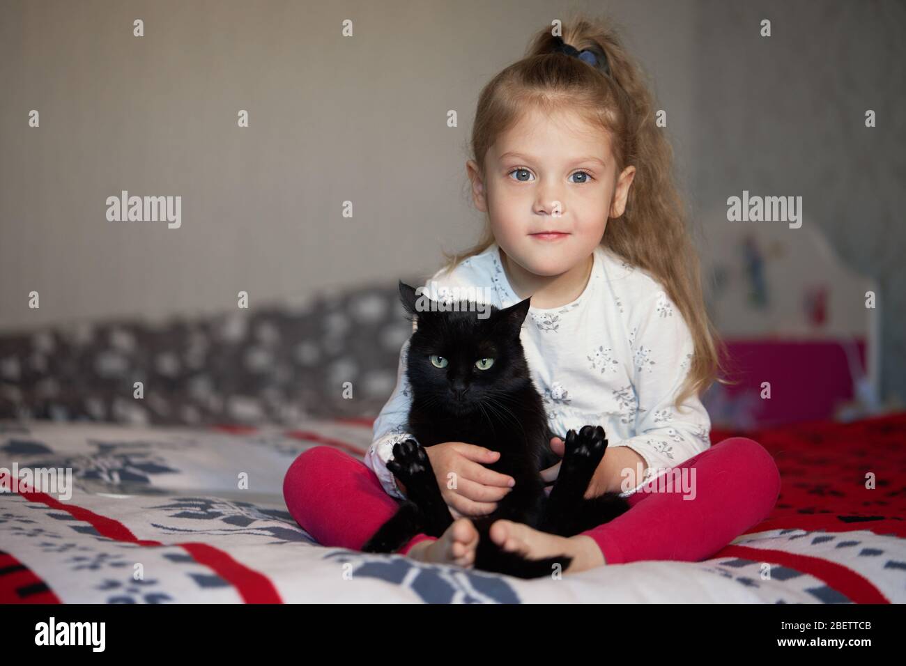 Portrait of a little cute child girl who hugs a black cat with tenderness and love and smiles with happiness Stock Photo