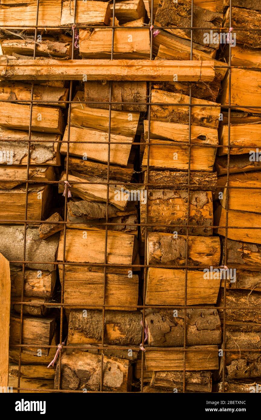 Woodpile of firewood chopped and stacked behind wall of mild steel mat Stock Photo