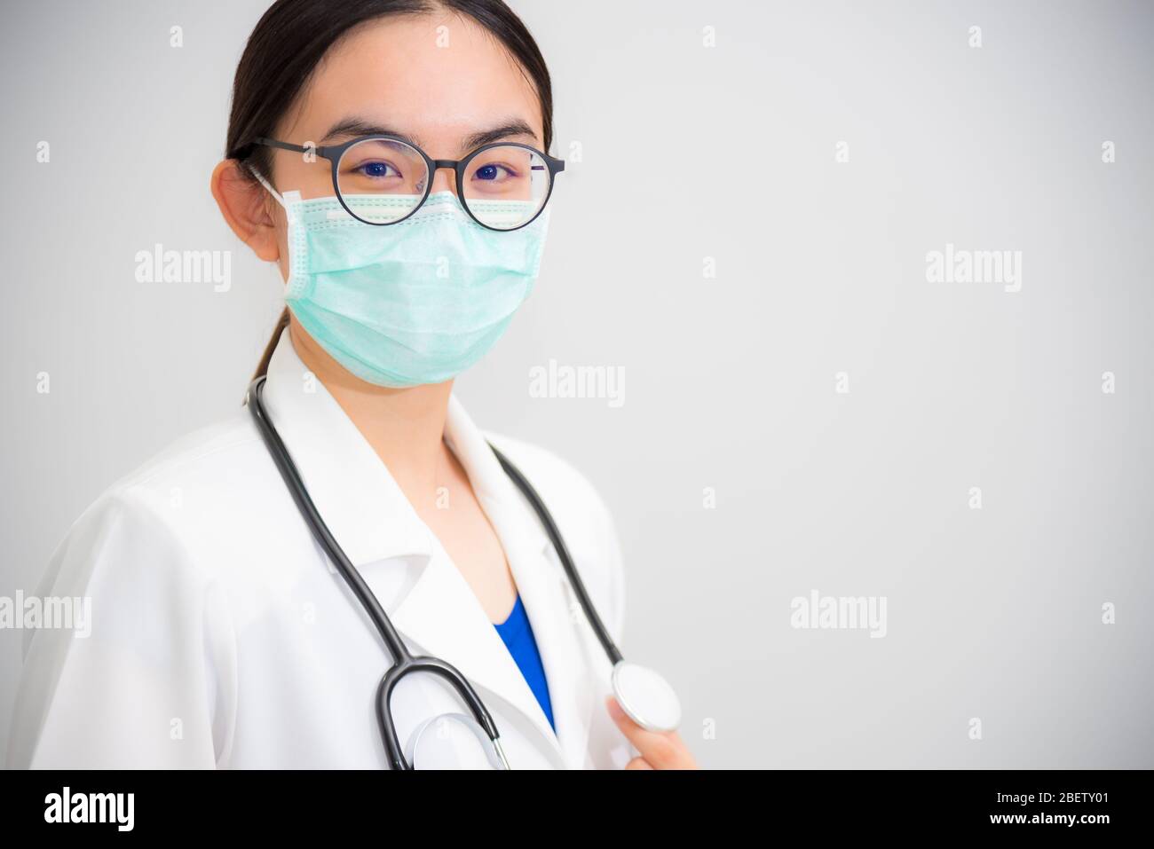 Studio portrait beautiful Asian young woman doctor with stethoscope in white uniform wear glasses and green mask to protect Corona Virus for health lo Stock Photo