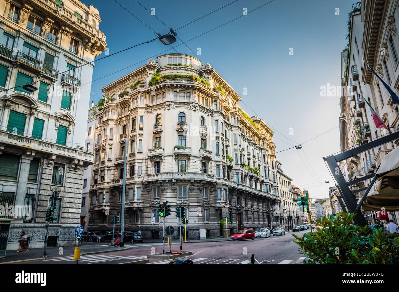 Corner of old typical building with balconies, windows, moulding, stucco work and greenery on roof on main street Corso Venezia in centre of Milan Mil Stock Photo