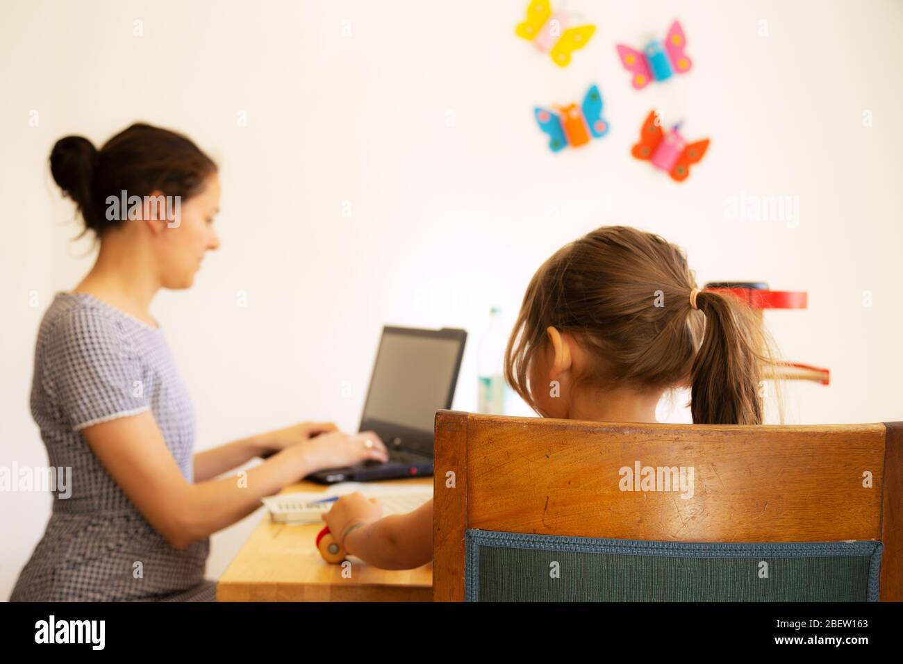 Businesswoman working in homeoffice with her daughter playing next to her during Covid-19 shutdown Stock Photo