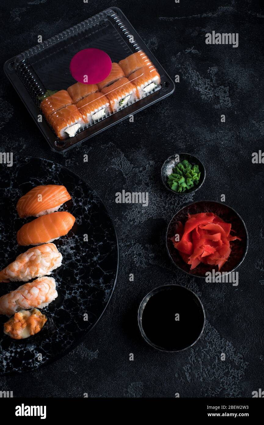 Delicious sushi set served on dark stone slate. Black background. Set of sushi rolls in plastic box, delivery service Stock Photo