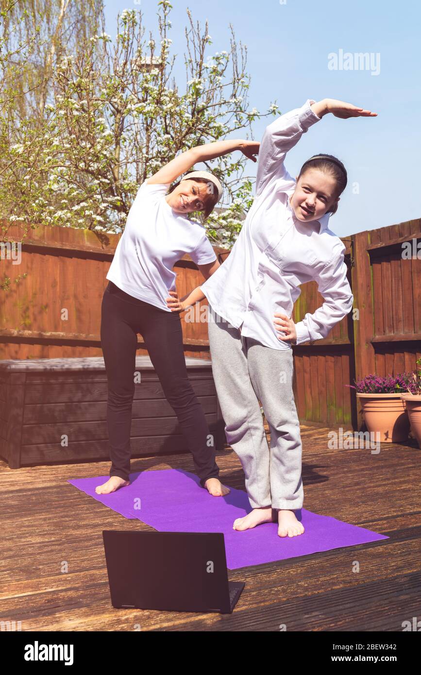 Happy Mother and Daughter are doing online yoga with laptop during self isolation at their back garden, no equipment workout, meditation tips for beginners, stay home and stay healthy concept Stock Photo