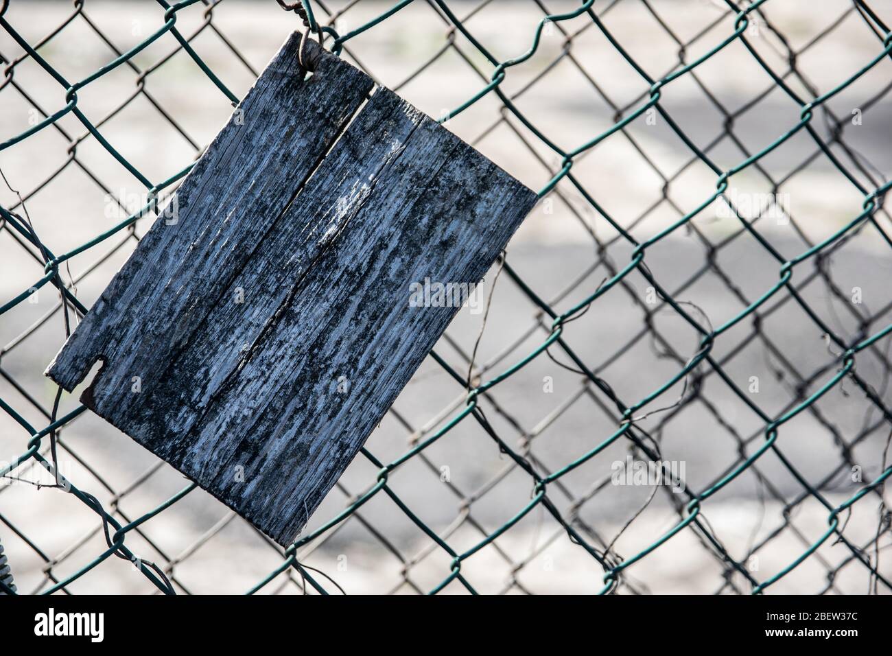 Old cracked rectangular wooden plate on an old green mesh fence Stock Photo