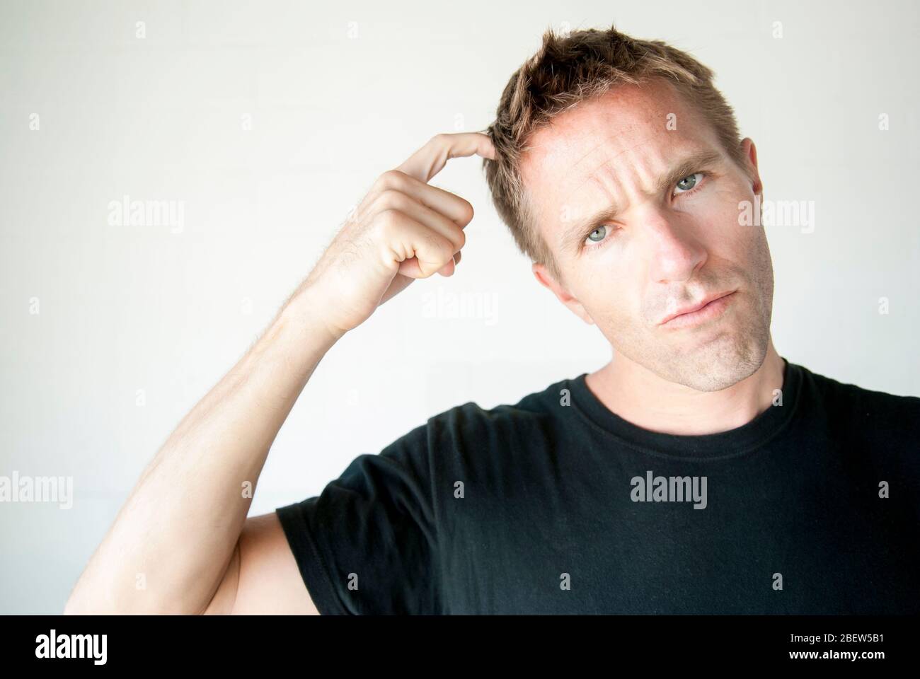 Casual young man in black T-shirt scratching his head looking at the camera with a pensive expression Stock Photo