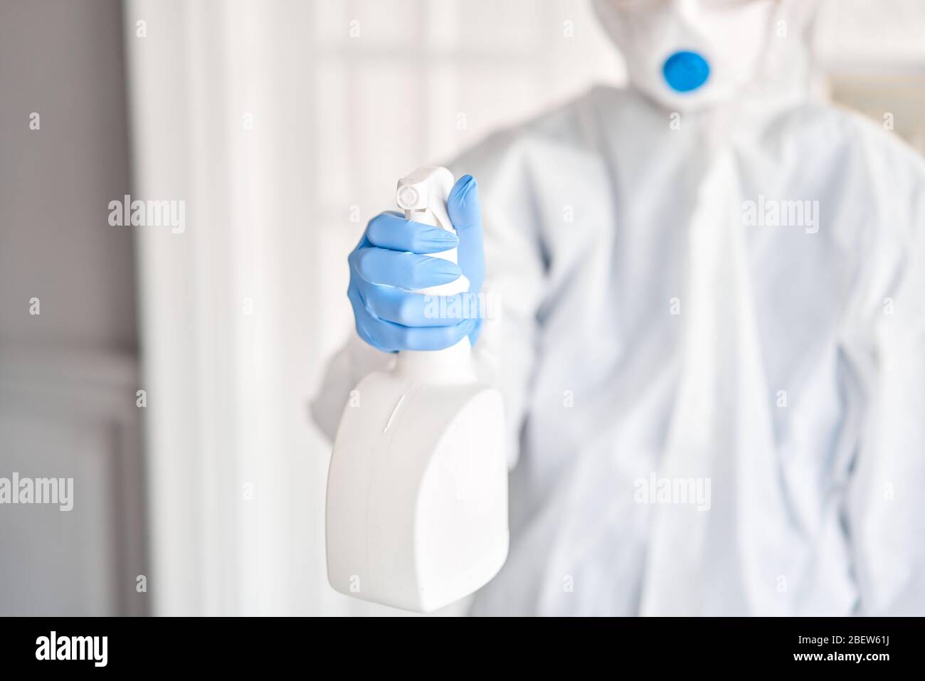 White spray bottle in woman hands in a protective suit and blue gloves. Disinfection, cleaning and washing. COVID-19. Prevention of coronavirus Stock Photo