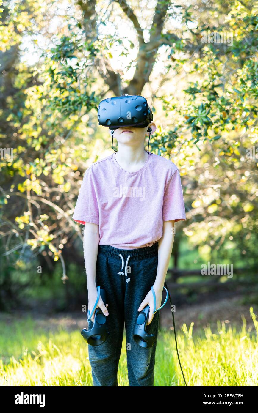 Young person standing in field in front of trees with VR goggles on Stock Photo