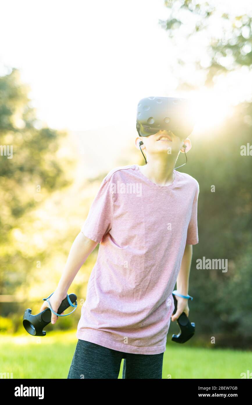 Tween having virtual experience with VR goggles outside in green field Stock Photo