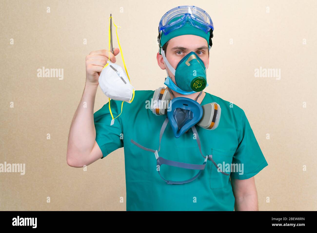 Doctor in green suit and respirator masks holds white medical respirator mask . Medical concept. Stock Photo
