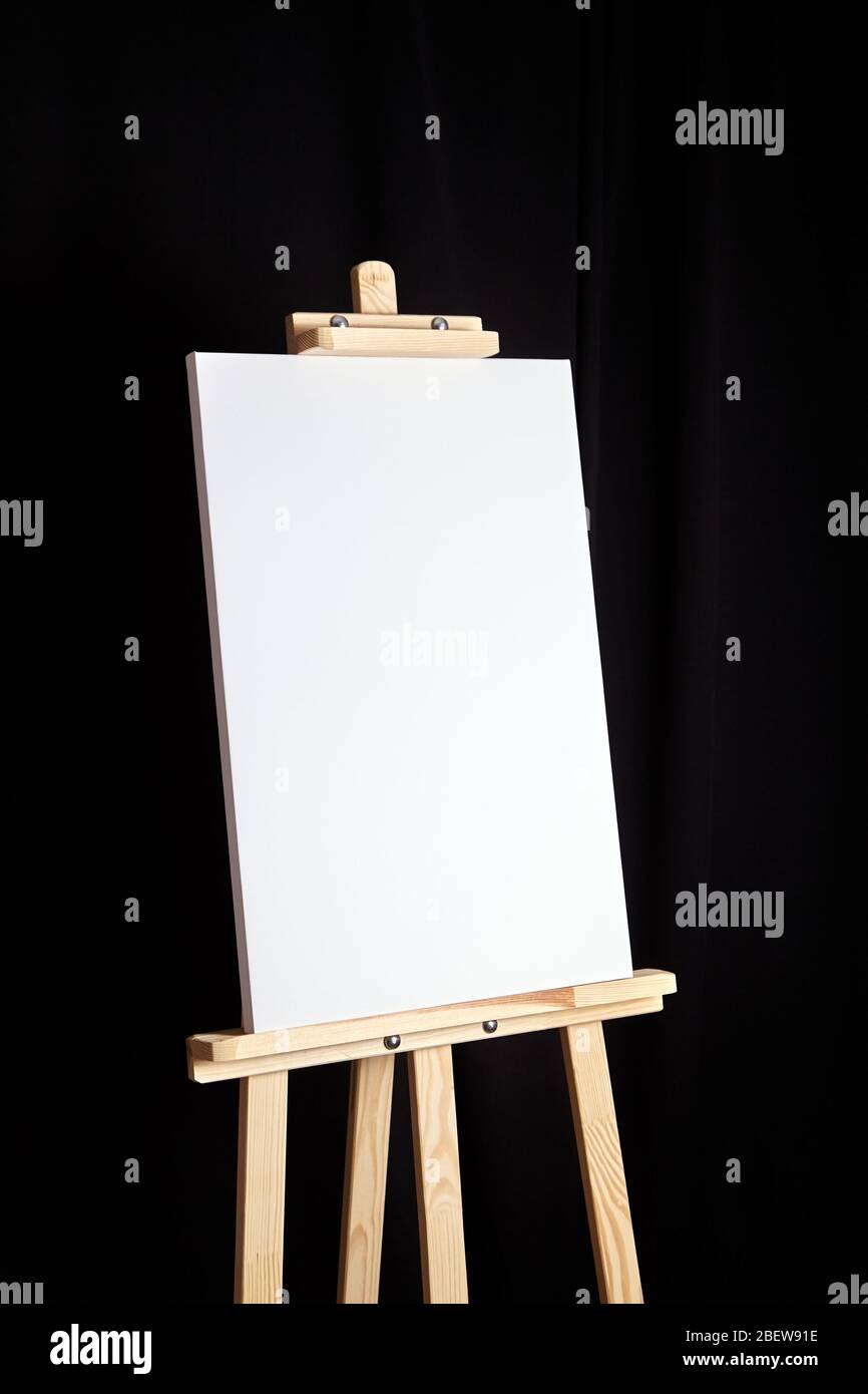 White blank canvas stands on a wooden artistic easel on black