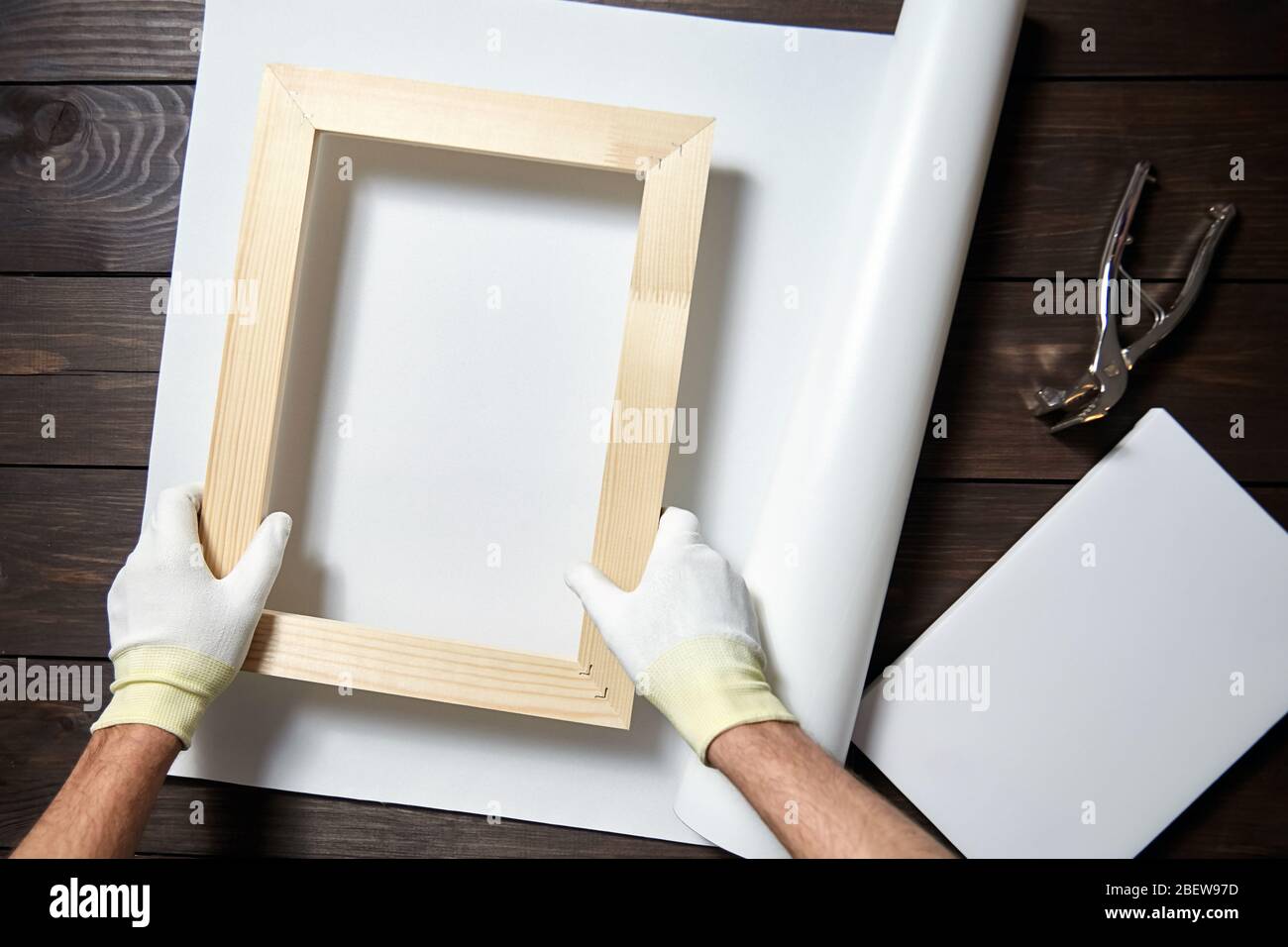 Canvas stretching process. Wooden stretcher bar, canvas pliers, male hand in white protect gloves Stock Photo